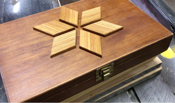 Old wooden box refreshed with oil and decorated with six raised contrasting wood pieces arranged in a star-shaped onlay design